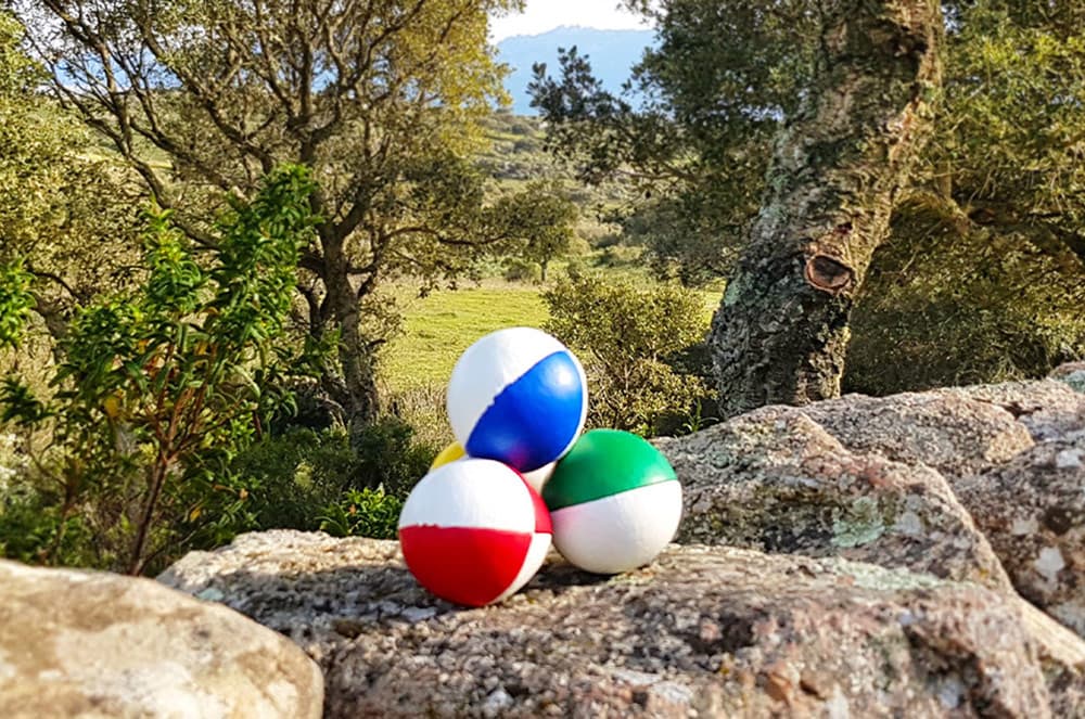Drei bunte Jonglierbälle auf einem Felsen vor einer sonnigen Baumlandschaft